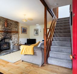 A living room with a stone fireplace and wood stove a gray sofa with a yellow blanket a television and carpeted stairs at Delfryn  Goginan in Goginan near Aberystwyth