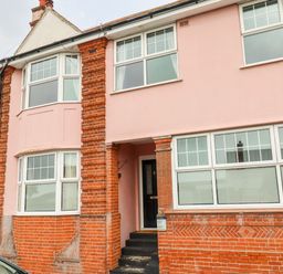 The front exterior of a two-story brick and pink painted house with multiple windows and a black front door at The Pink House in Felixstowe Suffolk