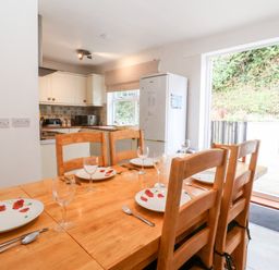 A dining table set with plates and glasses near a kitchen with cabinets and a refrigerator at The Pink House in Felixstowe Suffolk