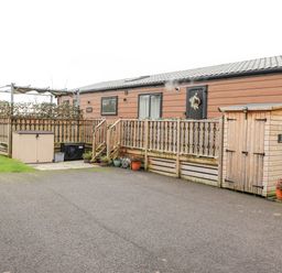 A wooden cabin with a fenced deck and a small shed in an outdoor area at Pine Lake View in Coniston View 3 Carnforth