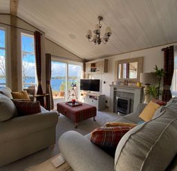 A living room with sofas a television and a fireplace overlooking a lake at Pine Lake View in Coniston View 3 Carnforth