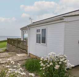Exterior of a white building with a wooden fence overlooking the sea and flowers in the foreground at Sealark in Eype