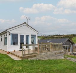 A small white house with a wooden deck and railing overlooking green hills at Sealark in Eype