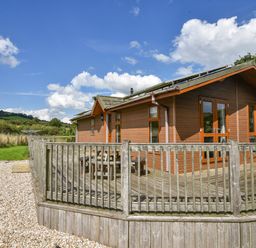 A wooden cabin with a fenced deck and outdoor table set in a rural area at The Hideaway in Eype