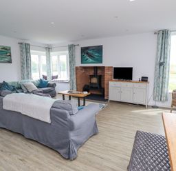 A living room with gray sofas a wood stove a TV on a cabinet and wicker chair at Turning Tide in Beadnell