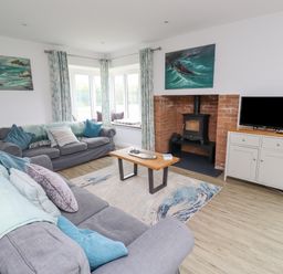 A living room with two sofas, a wooden coffee table, a wood burning stove, a TV on a sideboard and paintings on the walls at Turning Tide in Beadnell