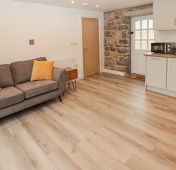 A living area with a gray sofa and yellow pillows next to a kitchen with white cabinets and a wooden door at The Stable in Amroth