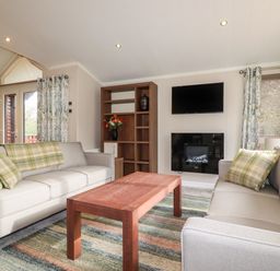 A living room with two sofas a wooden coffee table a wall-mounted TV and a fireplace at Haven Lodge Bossiney Bay near Tintagel