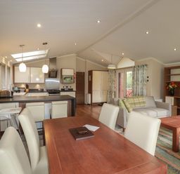 An open plan living space with a dining table and chairs kitchen area with island and stools and a sitting area with sofas and bookshelves at Haven Lodge in Bossiney Bay near Tintagel