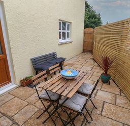 A small outdoor patio with a wooden table and chairs a bench and potted plants at The Loft @ Wisteria Cottage Saundersfoot