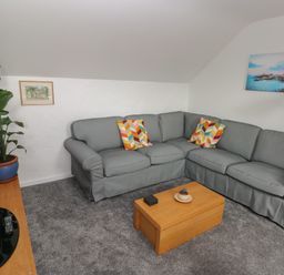 A living room with a gray corner sofa and colorful cushions a wooden coffee table a large green plant a flat screen tv and two wall pictures at The Loft @ Wisteria Cottage in Saundersfoot