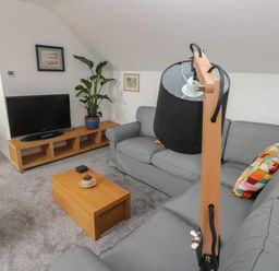 A living room with gray sofas a wooden coffee table a flat screen tv on a wooden stand and a floor lamp at The Loft @ Wisteria Cottage in Saundersfoot