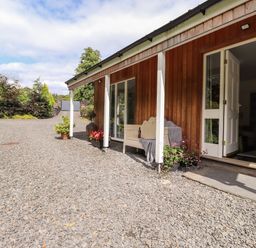 A gravel driveway alongside a wooden house with white pillars and an open door at Watersong Coniston