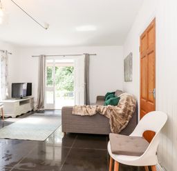 A living room with a sofa and throw blanket a chair a television and doors leading outside at Watersong in Coniston
