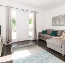 A living room with a grey sofa with green pillows a television on a white stand and a rug on the floor at Watersong in Coniston