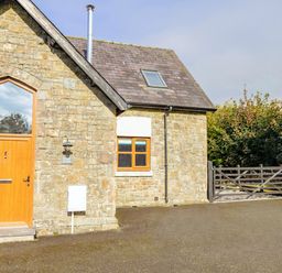 Stone house with wooden door and window next to a black wooden gate at School Lodge in Llandeilo