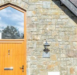 A wooden door and window on a stone wall with a lamp and a sign that reads School Lodge at School Lodge in Llandeilo