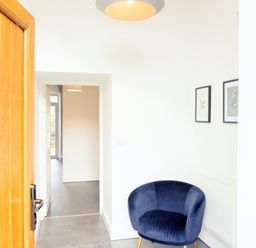 A hallway with a blue armchair next to a radiator and two framed pictures on the wall at School Lodge in Llandeilo