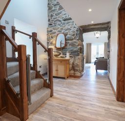 A hallway with wooden stairs carpeted with grey and a wooden cabinet with mirror near a stone wall at Gaerau Bach in Llanaber