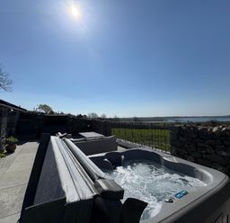 A patio with a hot tub seating area potted plants and stone walls overlooking a field and water at Gaerau Bach in Llanaber