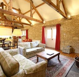 A living room with two sofas a wooden coffee table wooden beams and stone walls at The Granary in Bourton-On-The-Water