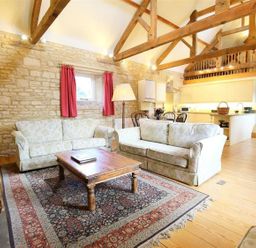 A living room with two patterned sofas a wooden coffee table and a rug under exposed wooden beams at The Granary in Bourton-On-The-Water
