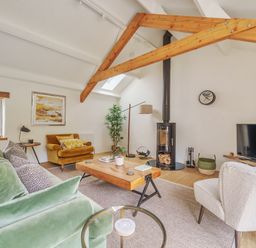 A living room with green sofa yellow armchair and white chair with wooden beams at The Granary in Davidstow near Camelford