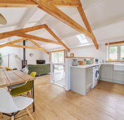 An open living space with wooden beams a dining table with chairs a green sofa a kitchen with appliances and windows at The Granary in Davidstow near Camelford