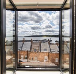 A view through open glass doors showing rooftops and a harbor with boats and a lighthouse visible at Casa Formentera in Scarborough
