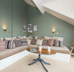 A living area with an L shaped cushioned bench with striped pillows and a wooden oval coffee table with two mugs and a magazine at Casa Formentera in Scarborough