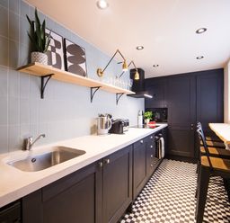 A kitchen with black cabinets a white countertop a black and white checkered floor and bar stools at Casa Formentera in Scarborough
