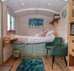 A small bedroom with a bed green chair wooden floor and wooden cabinets at Lottie's Hut in Okehampton