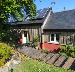 An exterior view of a wooden house with solar panels on the roof and a small outdoor seating area at The Studio at Dan y Garn in Newport Pembrokeshire