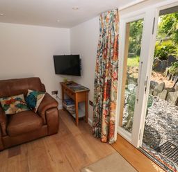 A small seating area with a brown leather armchair, a wooden side table with board games and a wall-mounted TV next to glass doors opening to a garden at The Studio at Dan y Garn in Newport Pembrokeshire