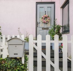 A front door with a floral wreath behind a white picket fence with a mailbox and plants at Moons Cottage in Fowey