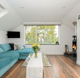 A living room with a blue sofa glass coffee table with flowers a fireplace and a large window at Moon's Cottage in Fowey