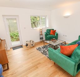 A sitting room with green sofa and armchair orange and blue cushions glass coffee table wooden floor and cabinet at James Place in Falmouth
