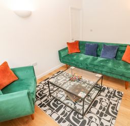 A sitting room with green sofas with orange and blue cushions a glass coffee table and a patterned rug at James Place in Falmouth