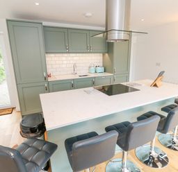 A kitchen with green cabinets a white countertop island with black bar stools and a black cooktop at James Place in Falmouth
