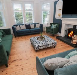 A living room with sofas and an armchair around a patterned ottoman and a fireplace at St Aidans in Alnwick