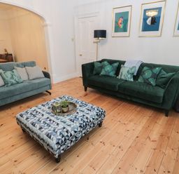 A living room with two sofas a patterned ottoman and framed bird prints on the wall at St Aidans in Alnwick