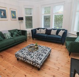 A living room with two green sofas a blue sofa a patterned ottoman and three bird pictures on the wall at St Aidans in Alnwick