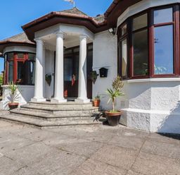 An entrance with white pillars and steps leading to a door with potted plants on a patio at Penang in St Austell