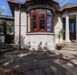 The exterior entrance of a house with a curved bay window columns and potted plants at Penang in St Austell