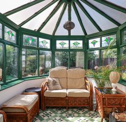 A conservatory with stained glass windows rattan furniture and a tiled floor at Penang in St Austell