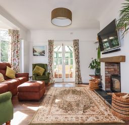 A living room with green and brown chairs a patterned rug a fireplace and a wall-mounted TV at Penang in St Austell