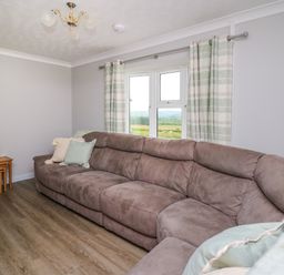 A living room with a large sectional sofa pillows stacked nesting tables and a window with curtains at Ashdale in Bwlch-y-sarnau near Rhayader