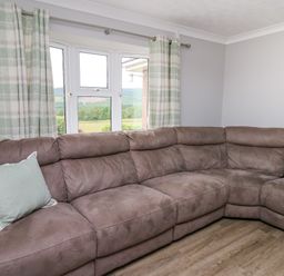 A living room corner with a large brown sectional sofa and green and cream plaid curtains at Ashdale in Bwlch-y-sarnau near Rhayader
