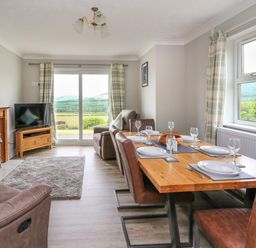 A dining table set with plates and glasses in a room with leather chairs a fireplace a television and sliding glass doors overlooking fields at Ashdale in Bwlch-y-sarnau near Rhayader