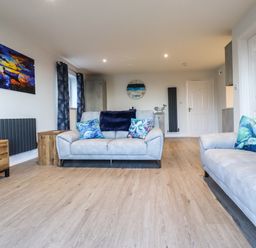 A living room with two sofas and colorful pillows a wooden cabinet and paintings at 2A The Anchorage in Beadnell